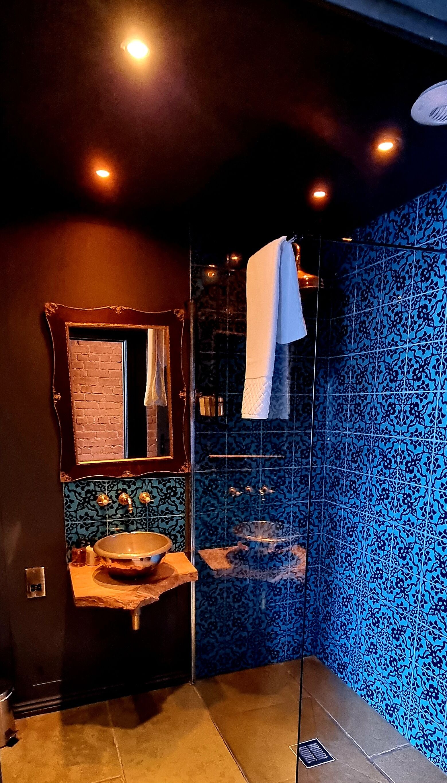 A bathroom with a large mirror, a sink with a bowl, and a shower area with blue patterned tiles.
