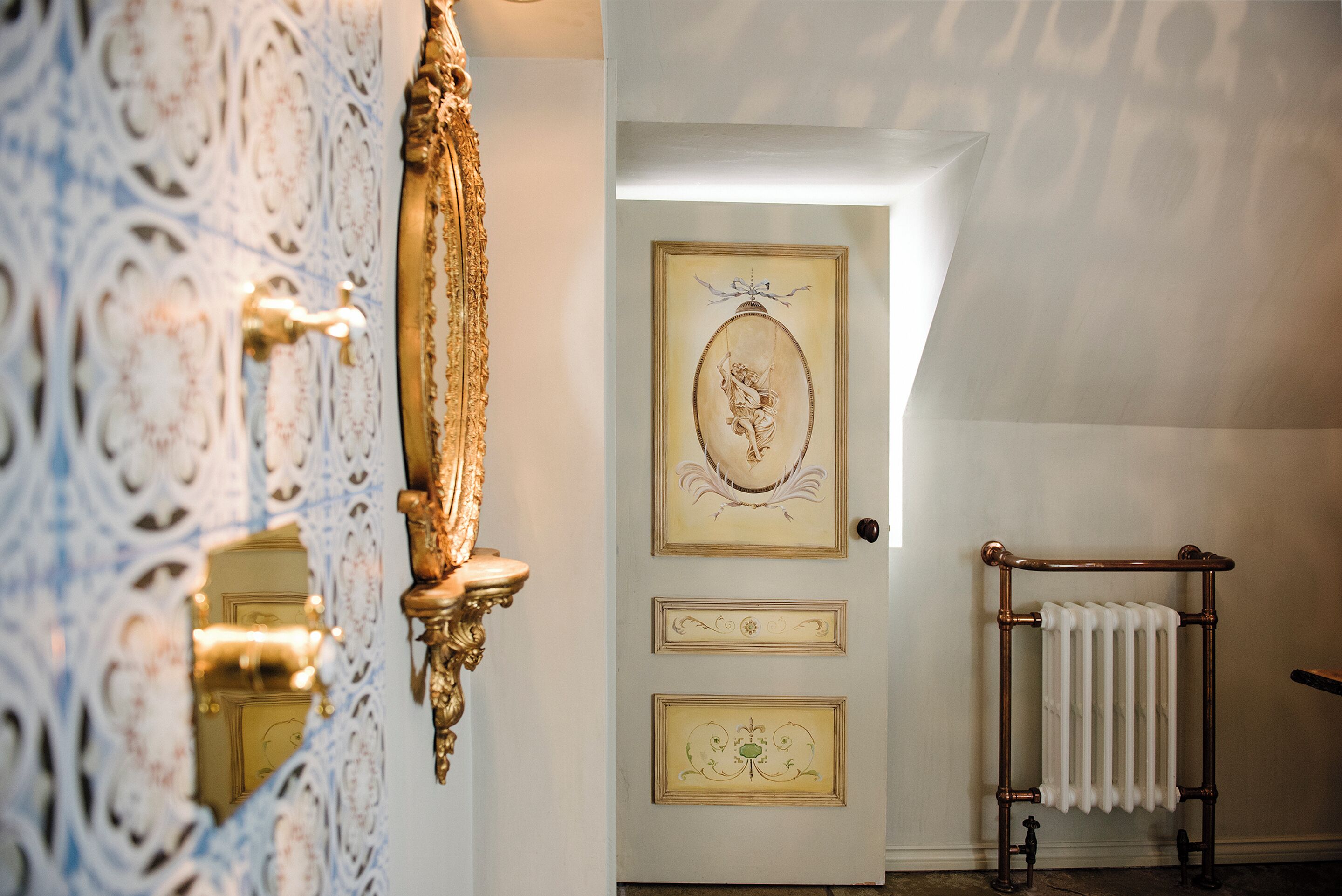 A room with ornate wallpaper, a door with decorative panels, and a radiator.