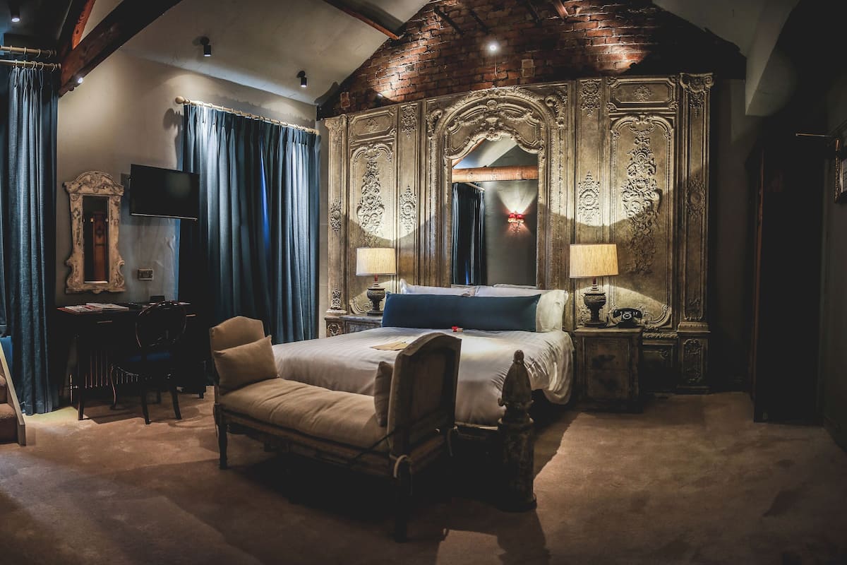 Une chambre à coucher luxueuse avec un grand lit, un fauteuil classique, un bureau avec une lampe et un miroir.