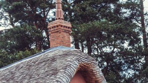 A quaint house with a thatched roof, a brick chimney, and a wooden door with decorative panels. -  Le Petit Chateau & William de Percy (Newcastle-upon-Tyne)