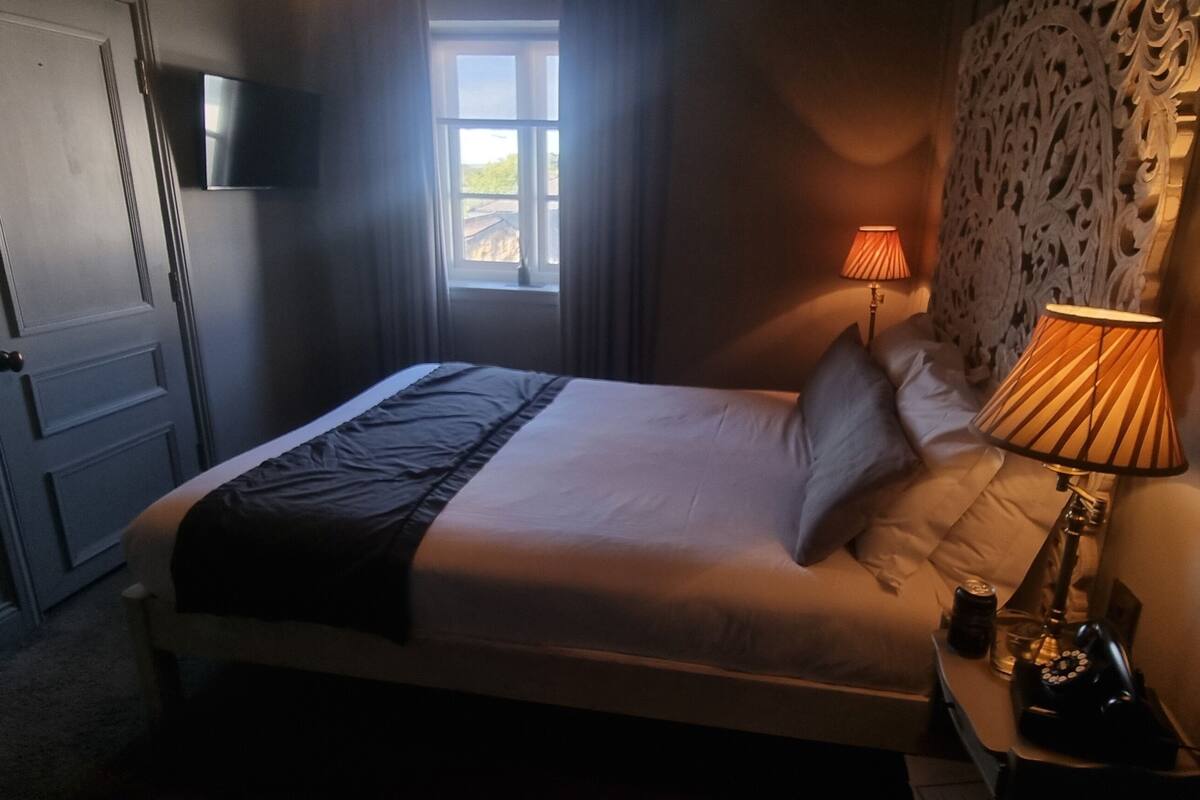 Une chambre à coucher avec un lit, une lampe de chevet, une fenêtre et un téléviseur fixé au mur.