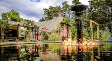 A house with a thatched roof, a fountain, and a pond reflecting the surroundings.