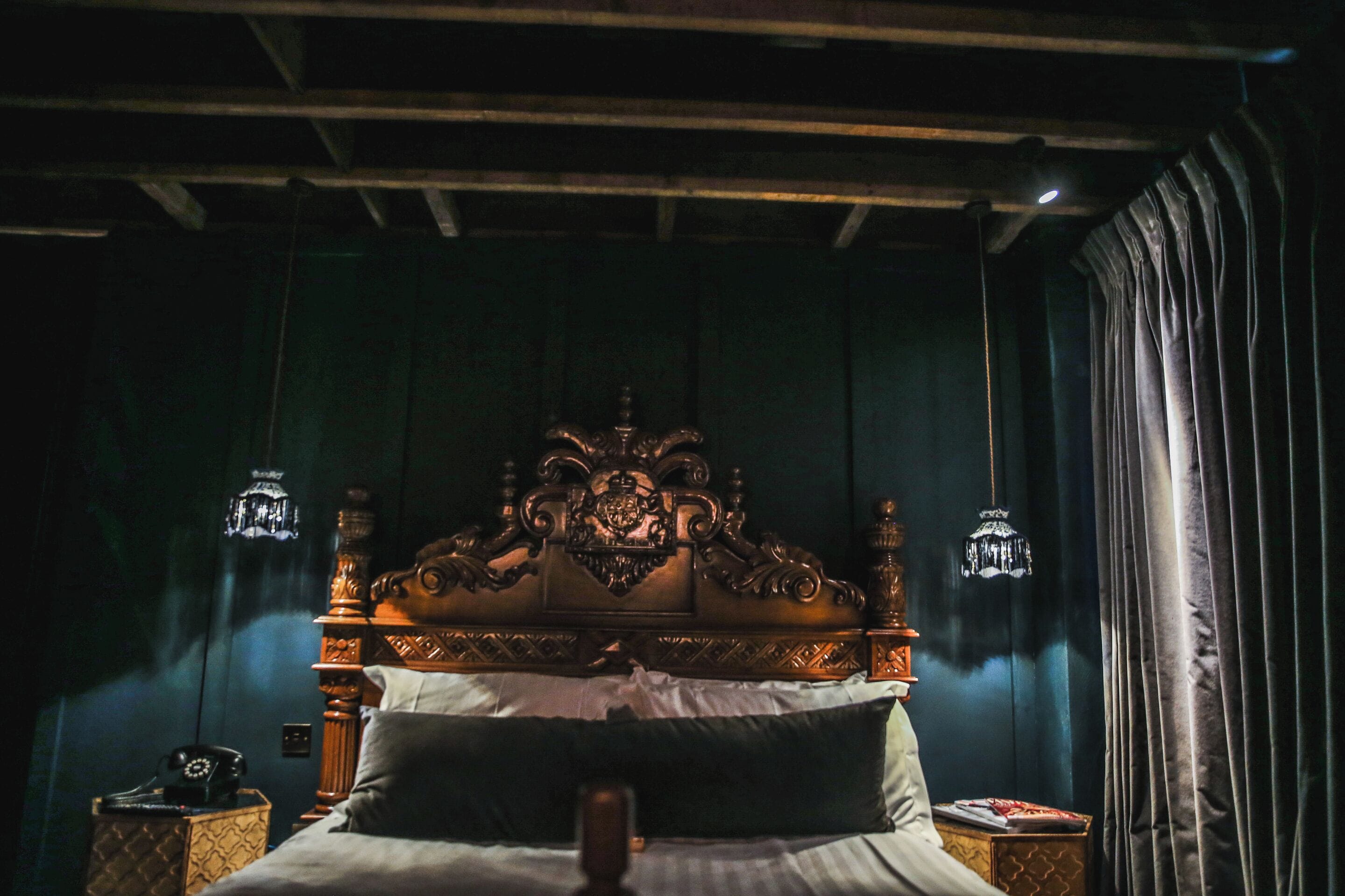 A bedroom with a wooden headboard, a bedside table with a lamp, and a curtain.