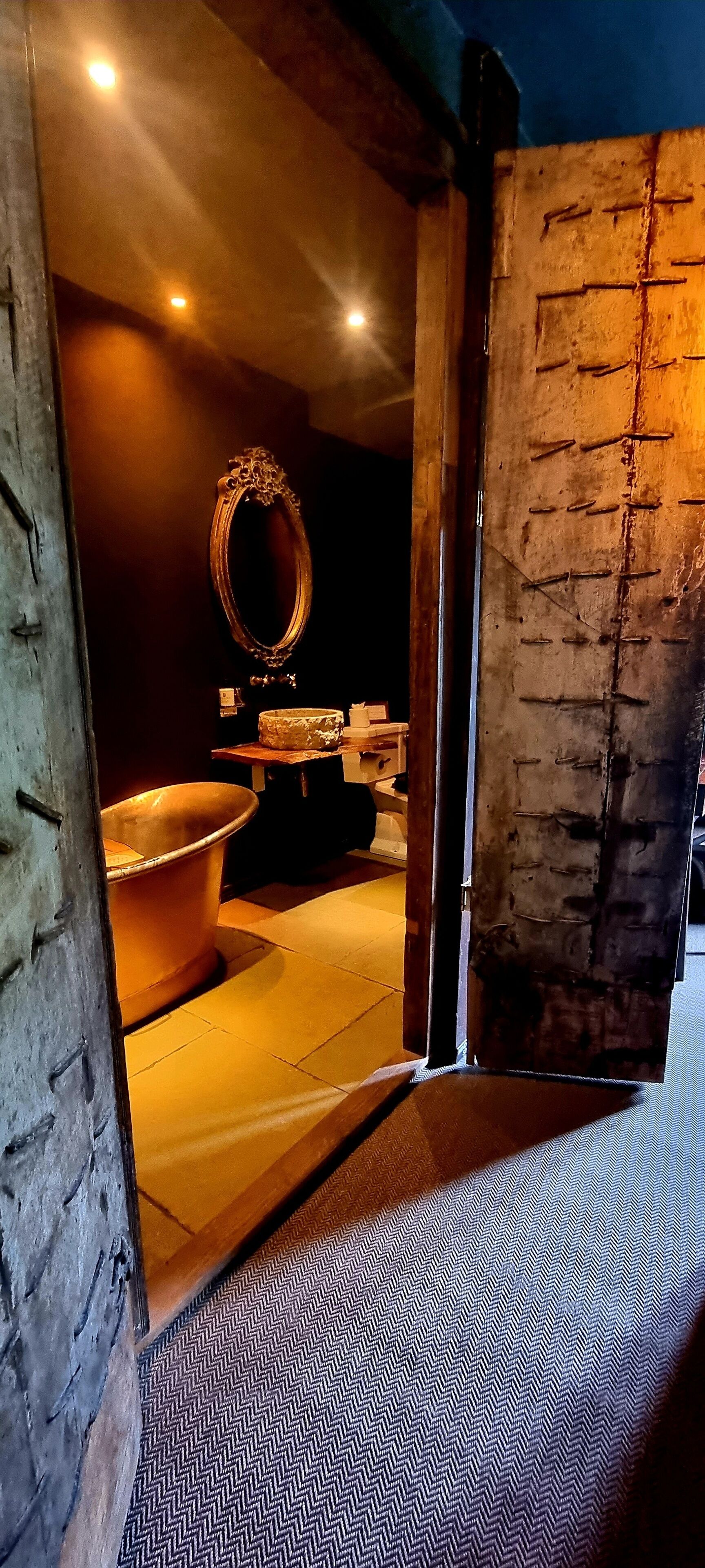 An interior view of a bathroom with a large bathtub, a mirror, and a wooden door.