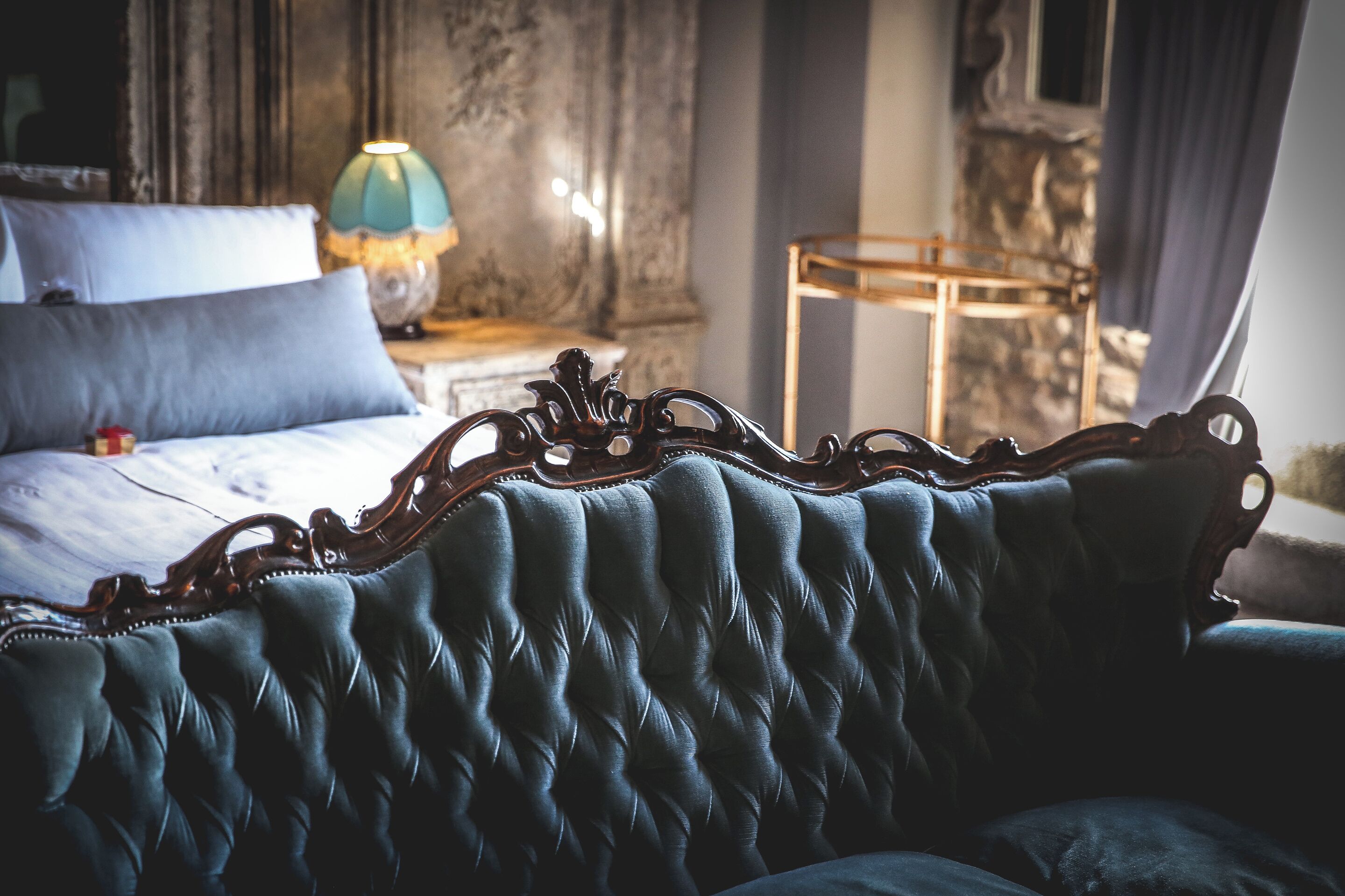 Una habitación con un sofá azul con capitonado, una cama con ropa de cama azul, una lámpara y una pared de piedra.