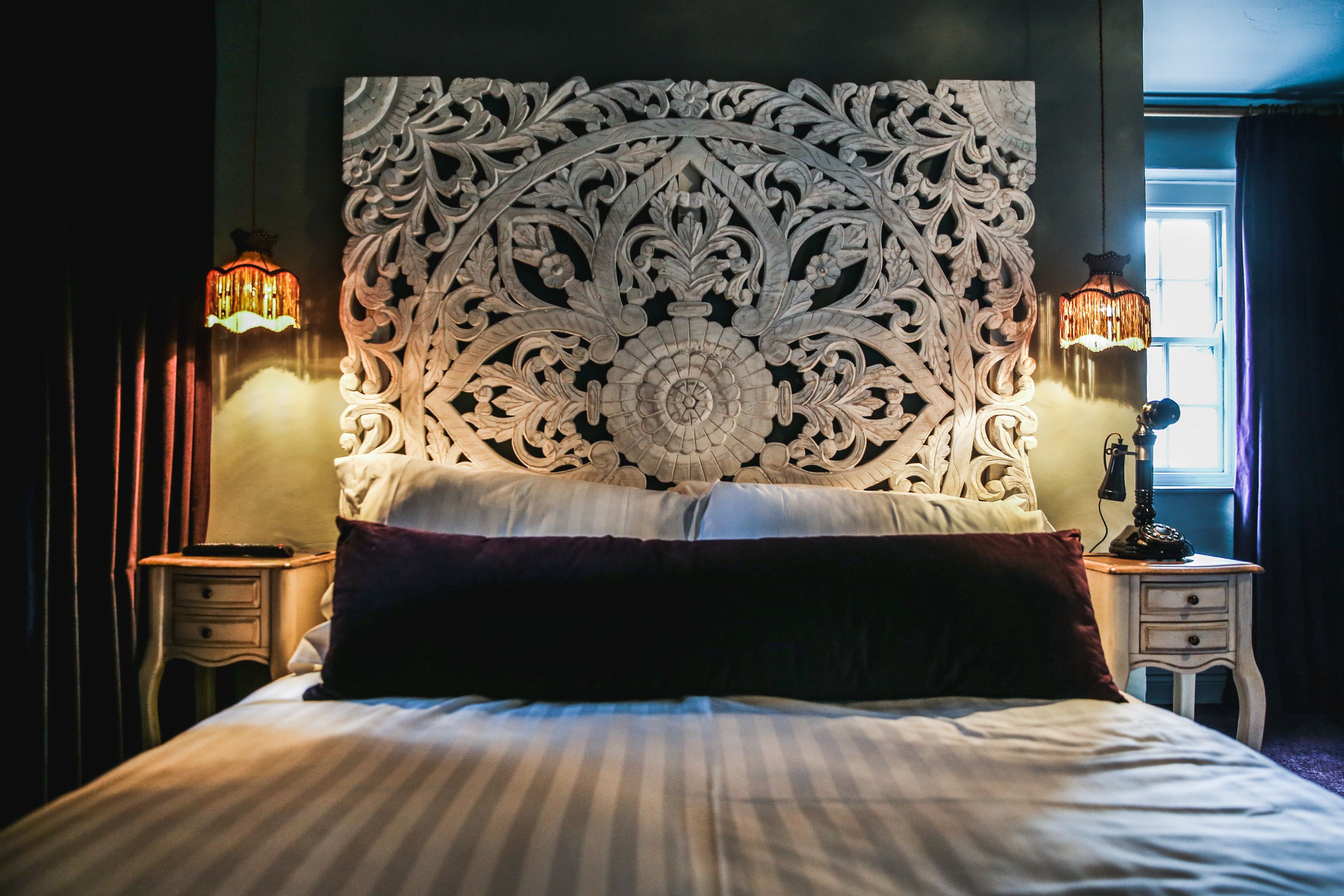 A bed with a decorative headboard, two bedside lamps, and a nightstand with a telephone.
