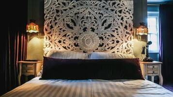 A bed with a decorative headboard, two bedside lamps, and a nightstand with a telephone.
