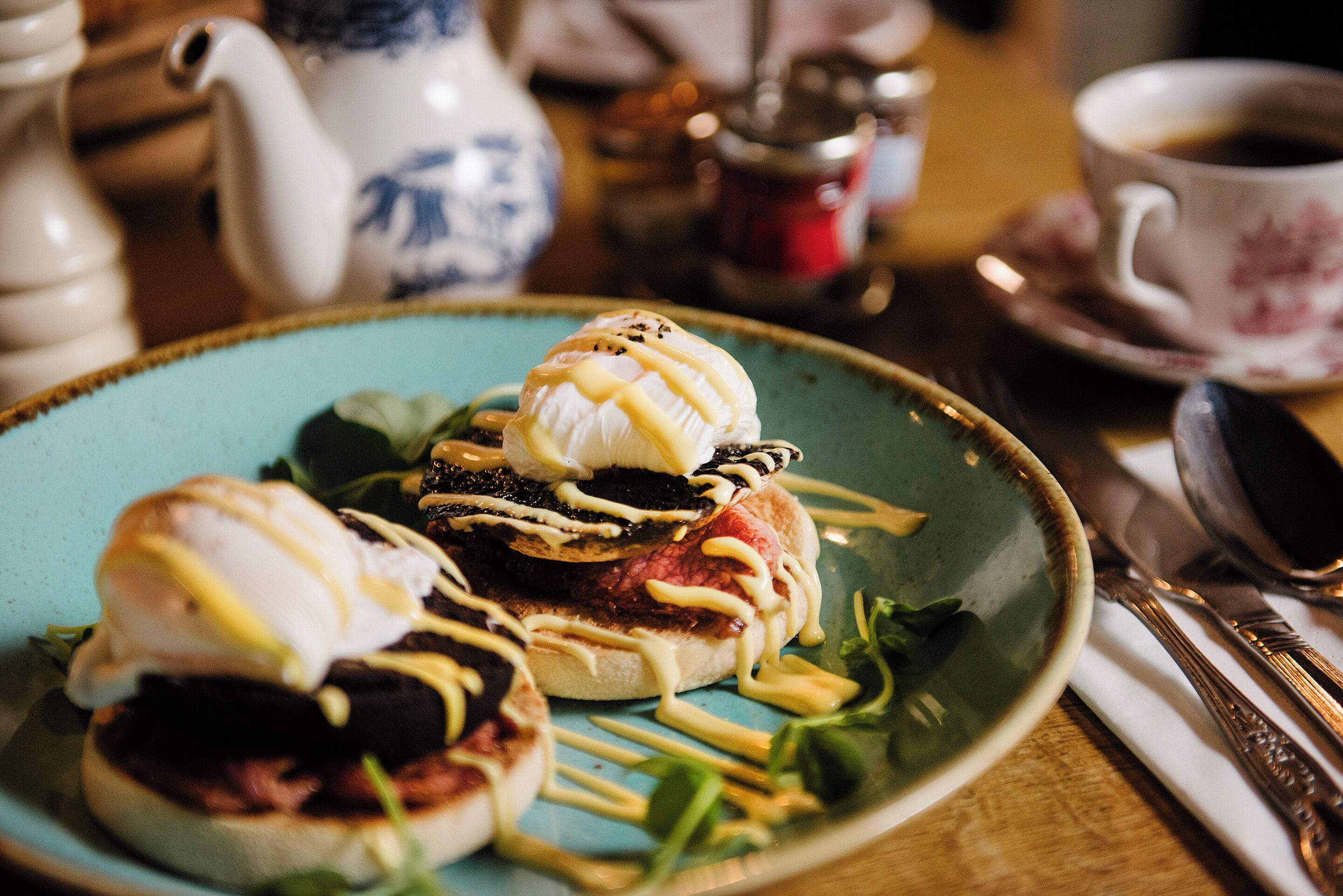 A plate with a breakfast dish, a teapot, and a cup of coffee on a table.