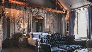 A room with a bed, a blue upholstered sofa, a small table, and a lamp. -  Le Petit Chateau & William de Percy (Newcastle-upon-Tyne)