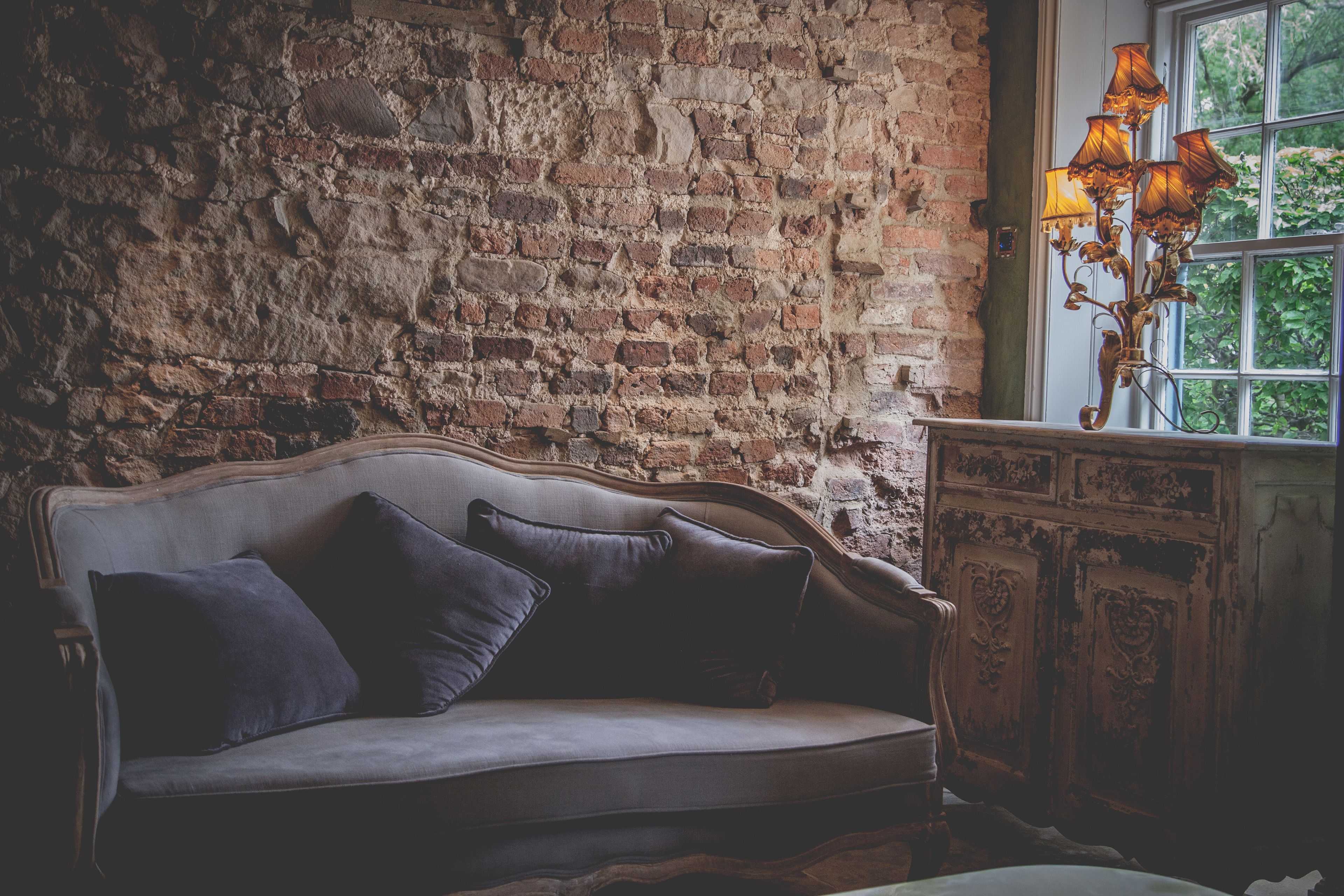 Een kamer in vintage stijl met een bakstenen muur, een houten kast en een met kussens beklede bank.