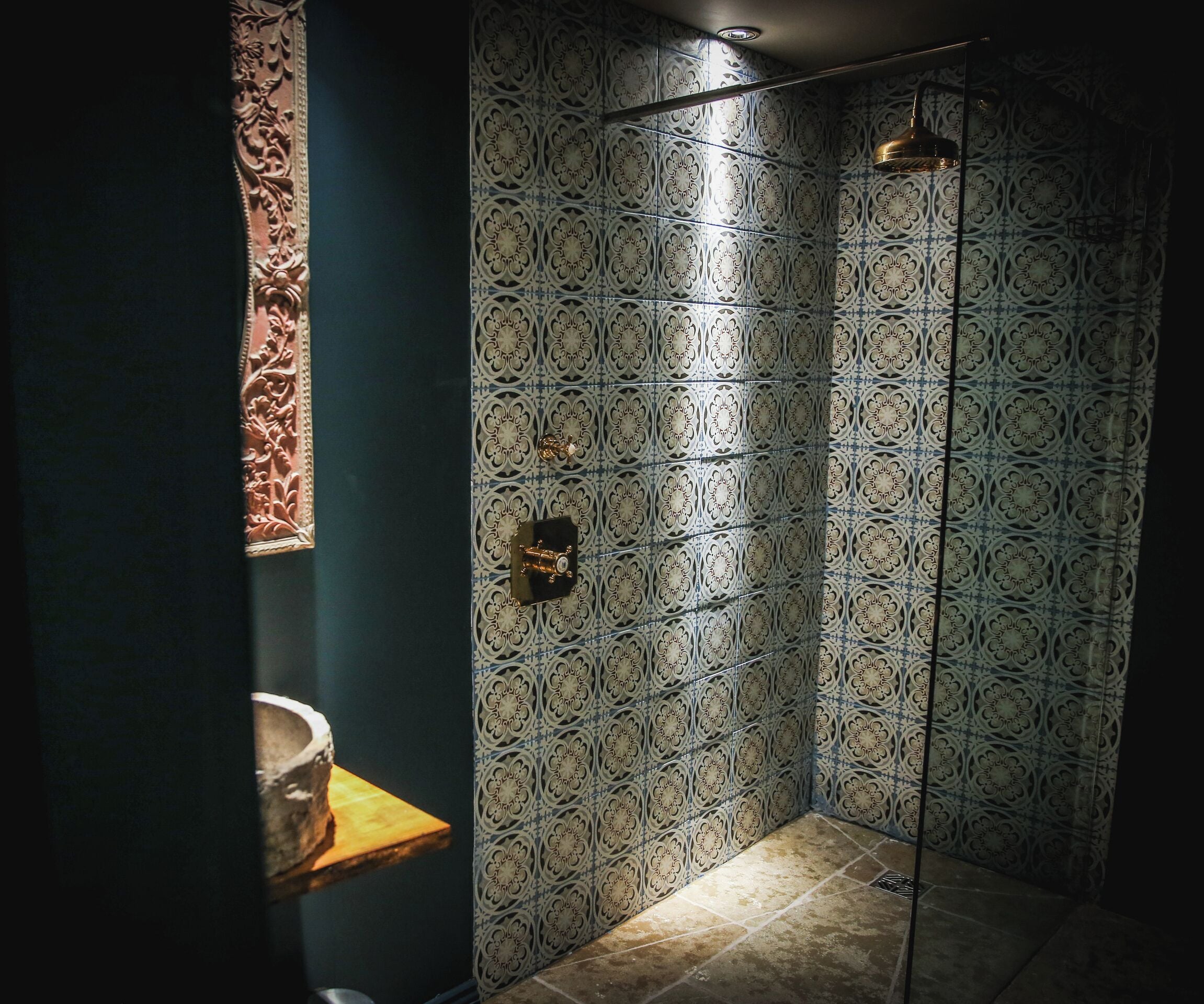 A bathroom with patterned tiles, a shower, and a wooden shelf.