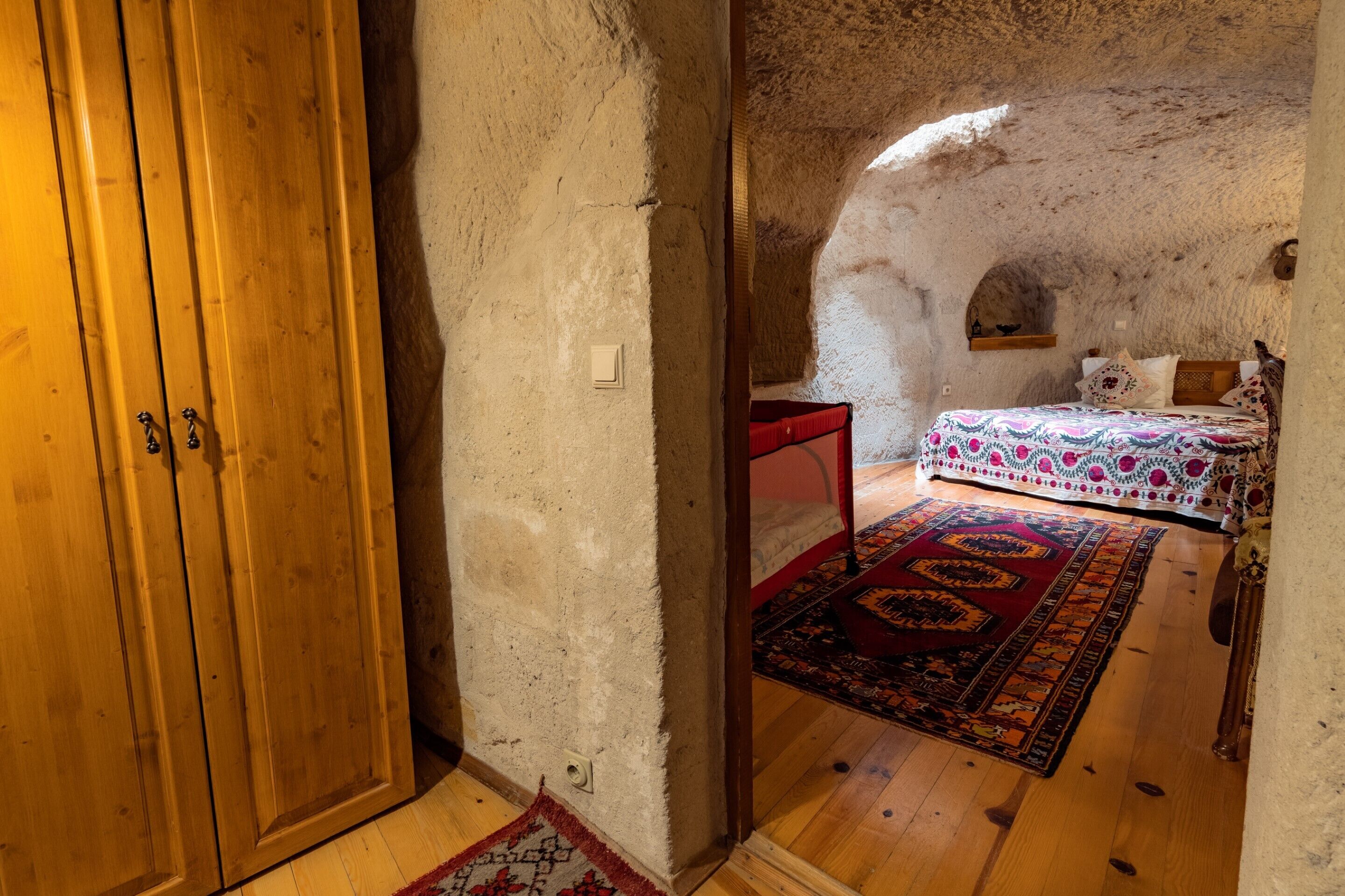 A rustic room with a wooden wardrobe, a bed with patterned bedding, and a red bench.