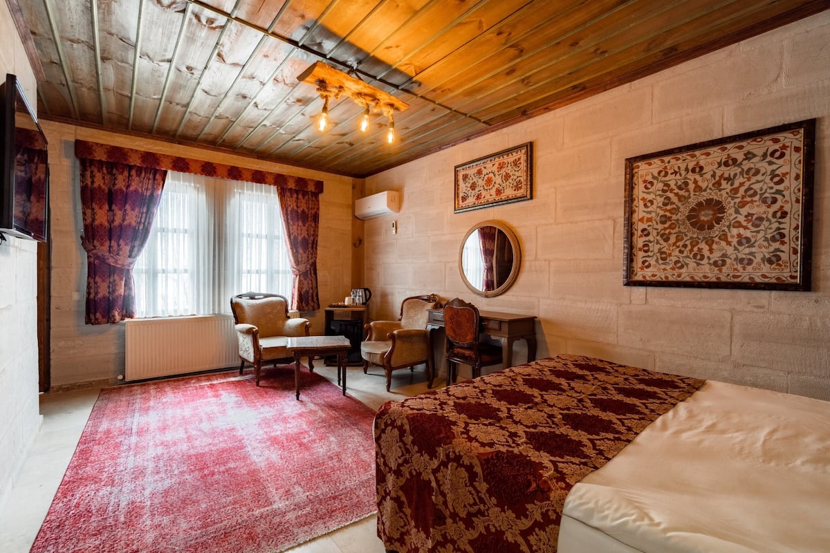 A cozy room with a wooden ceiling, a bed, a desk, a chair, and a radiator.