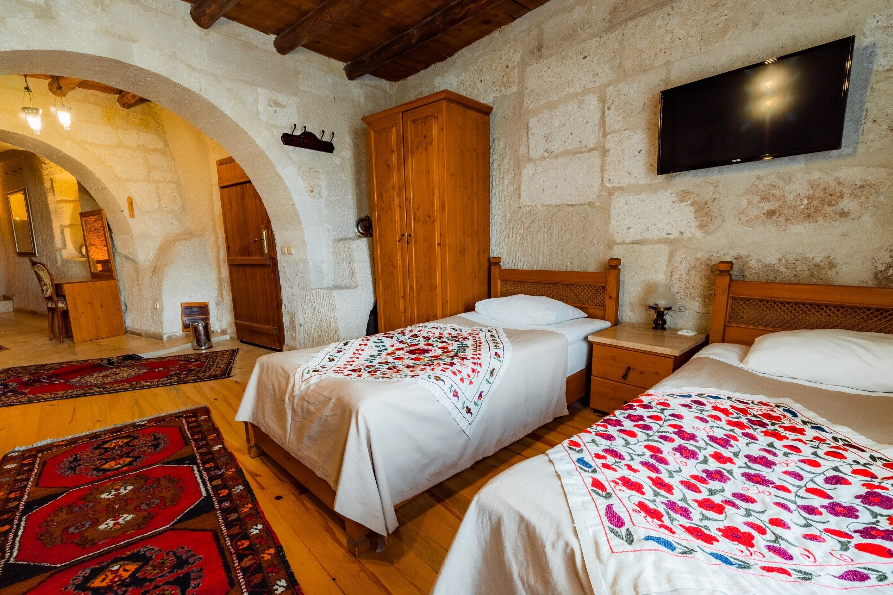 A traditional room with a stone wall, wooden furniture, a TV, and two beds with patterned bedspreads.