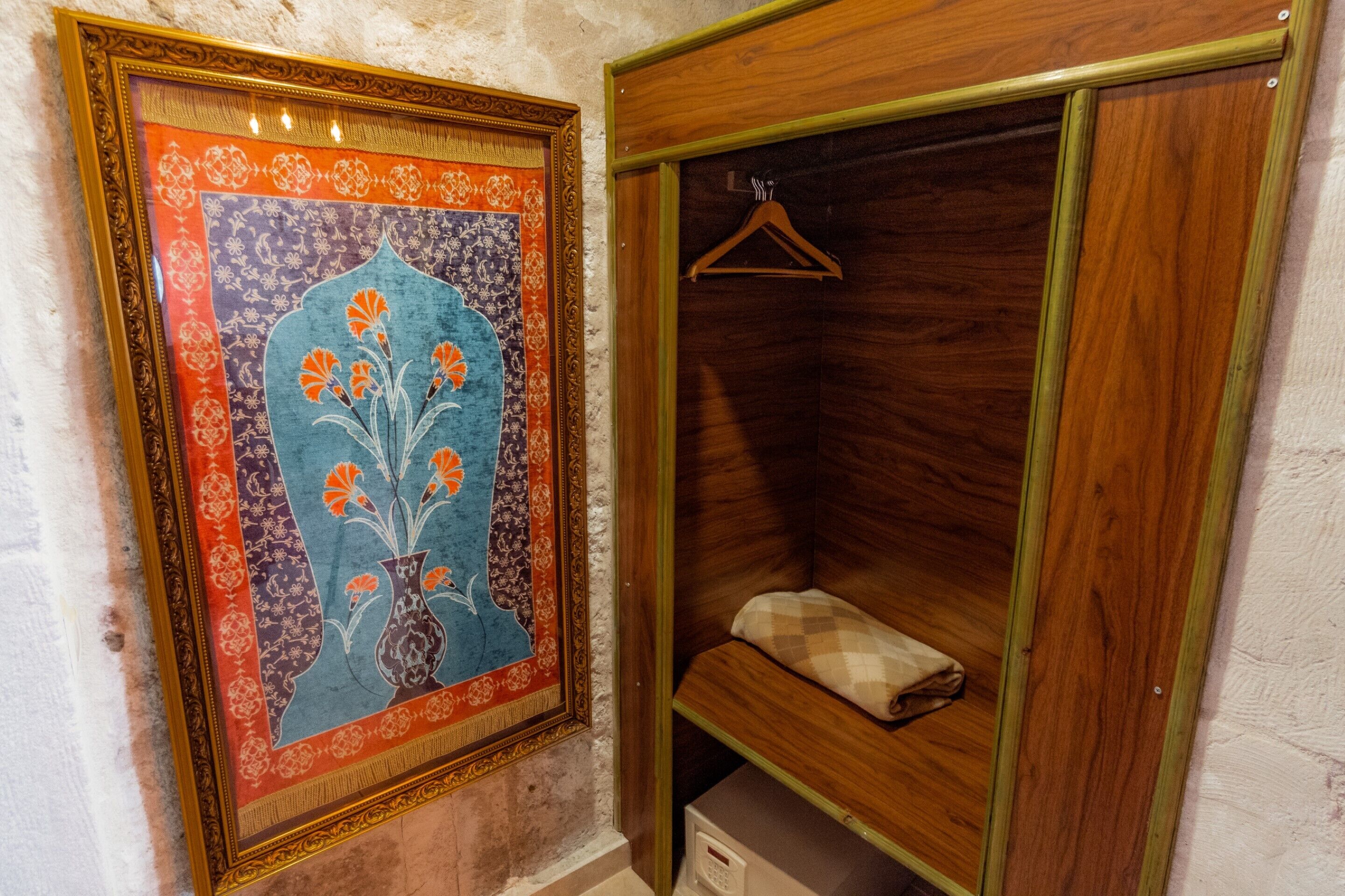 A room with a framed artwork on the wall, a wooden wardrobe, and a hanging garment.
