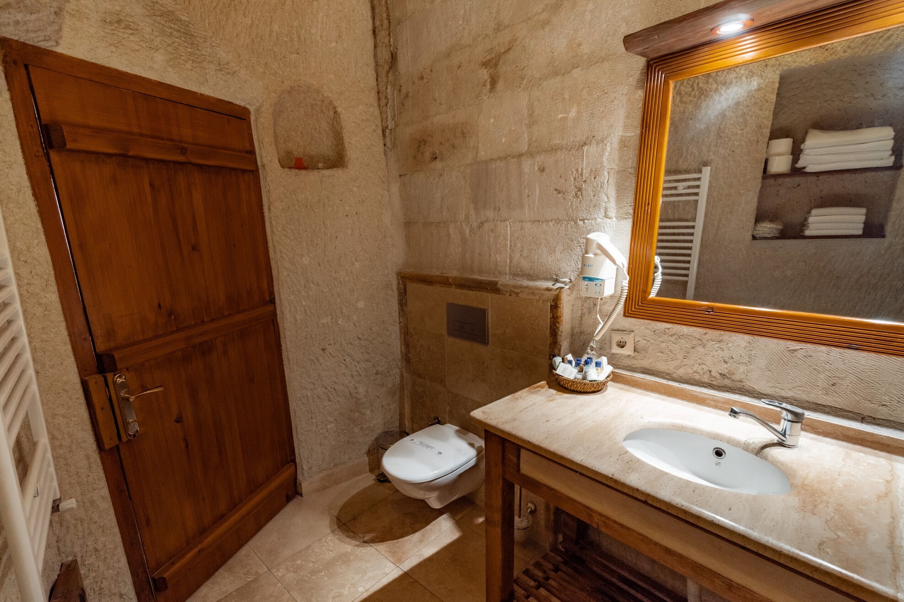 A bathroom with a wooden door, a toilet, a sink, and a mirror.