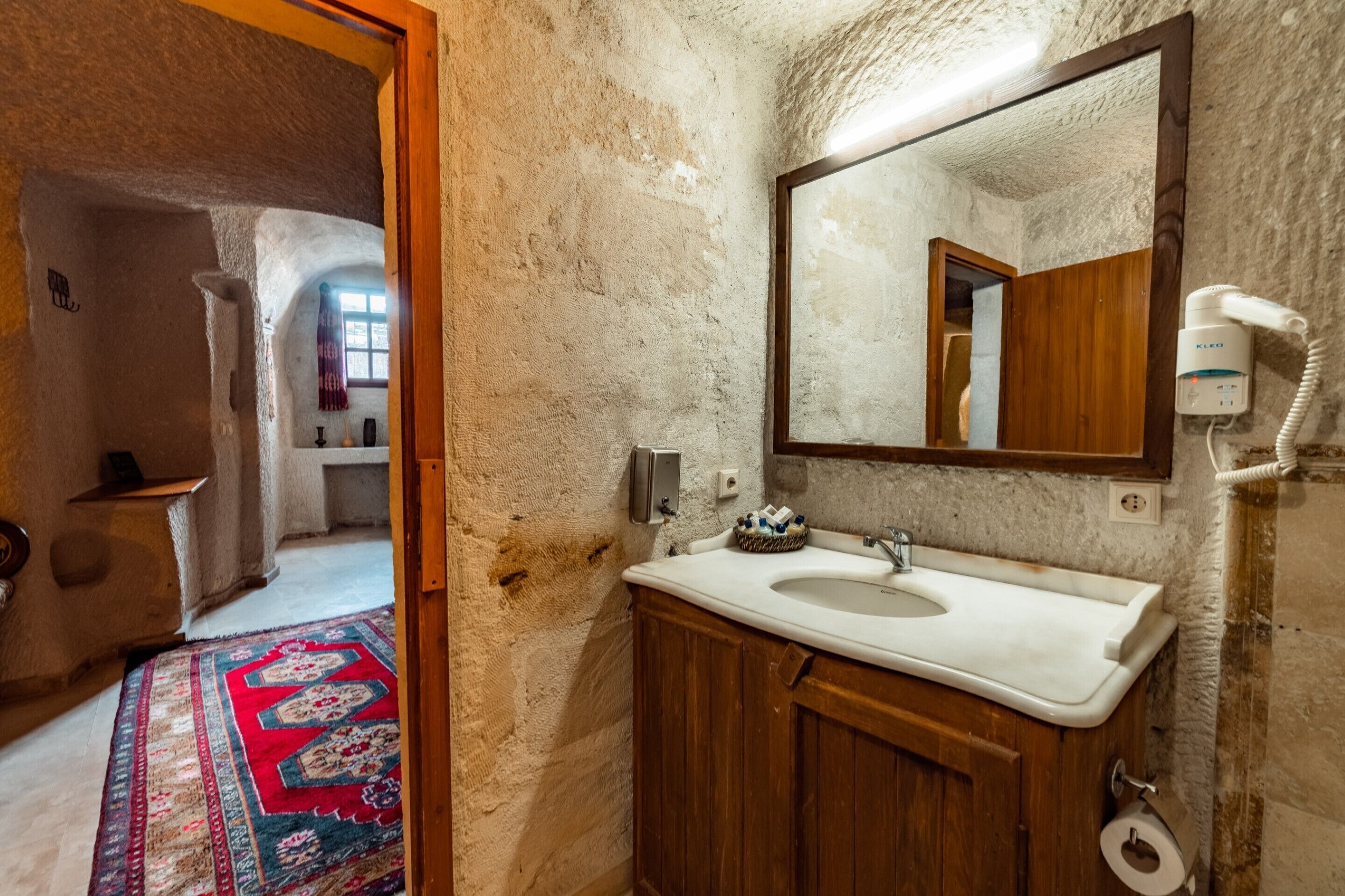 A rustic bathroom with a stone wall, wooden cabinet, and a large mirror.