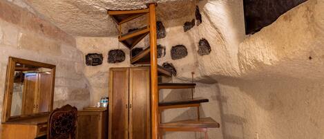 A room with a spiral staircase, wooden furniture, a mirror, and stone walls.