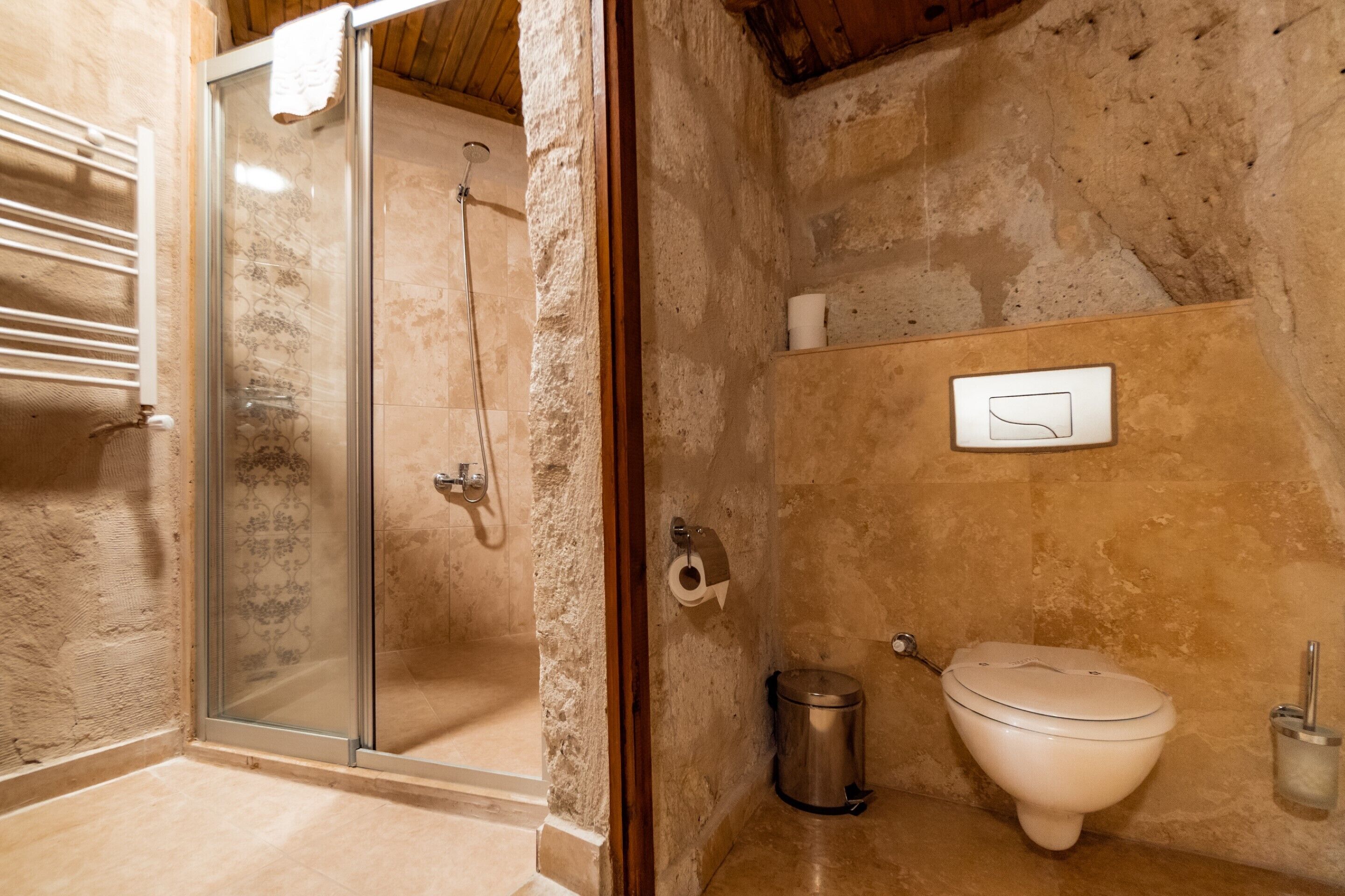A bathroom with a glass-enclosed shower, a toilet, and a trash can.