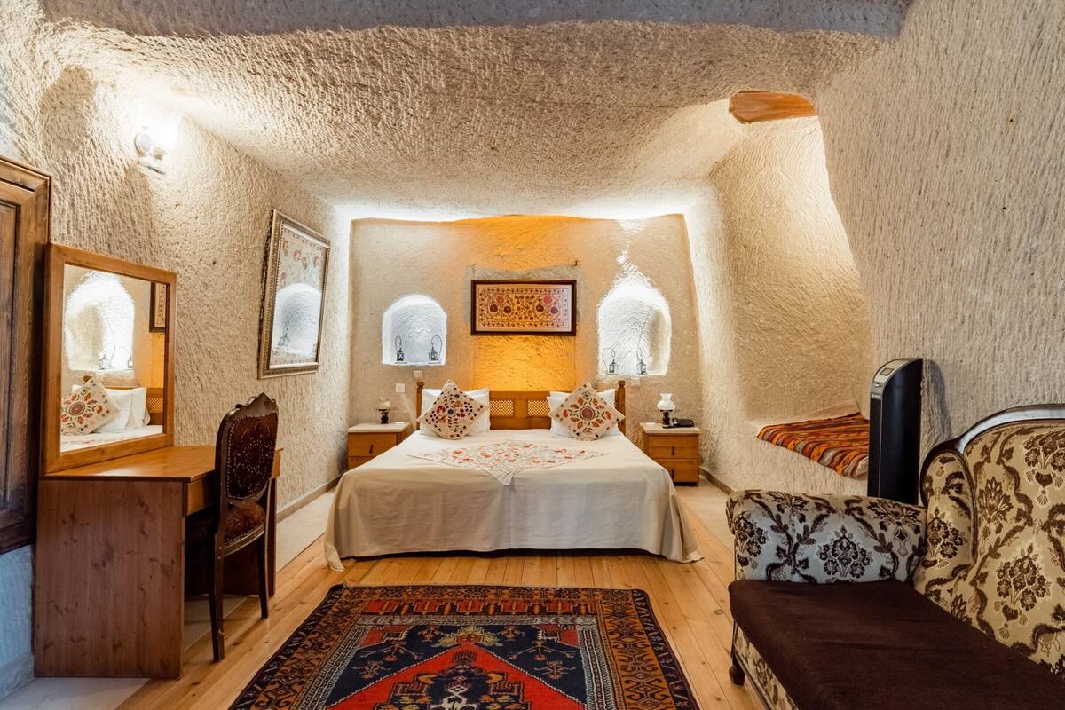 A bedroom with a large bed, two bedside tables, a wooden desk, a chair, and a patterned rug.