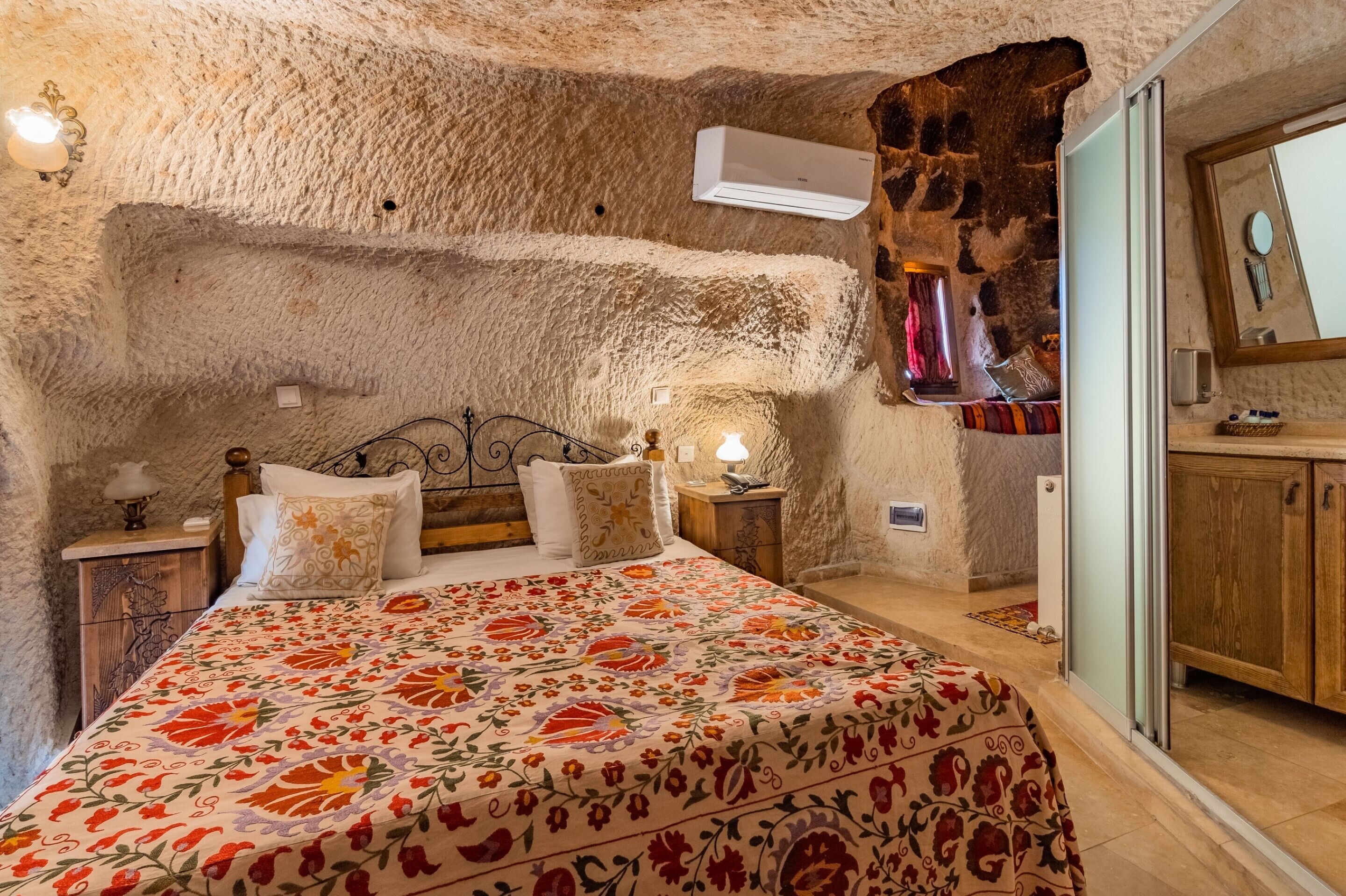A bedroom with a stone wall, a bed with floral bedding, a nightstand with a lamp, and a wooden cabinet.