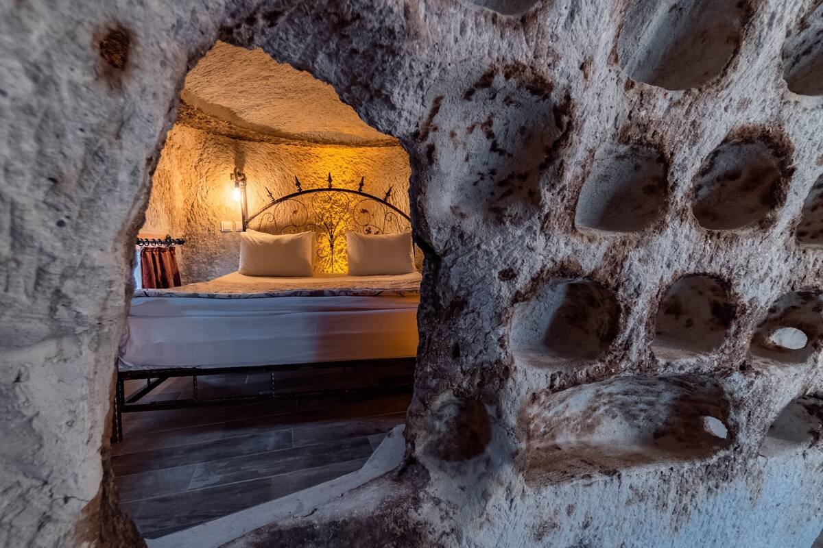 A cozy room with a bed, a wall-mounted lamp, and a rustic stone wall.