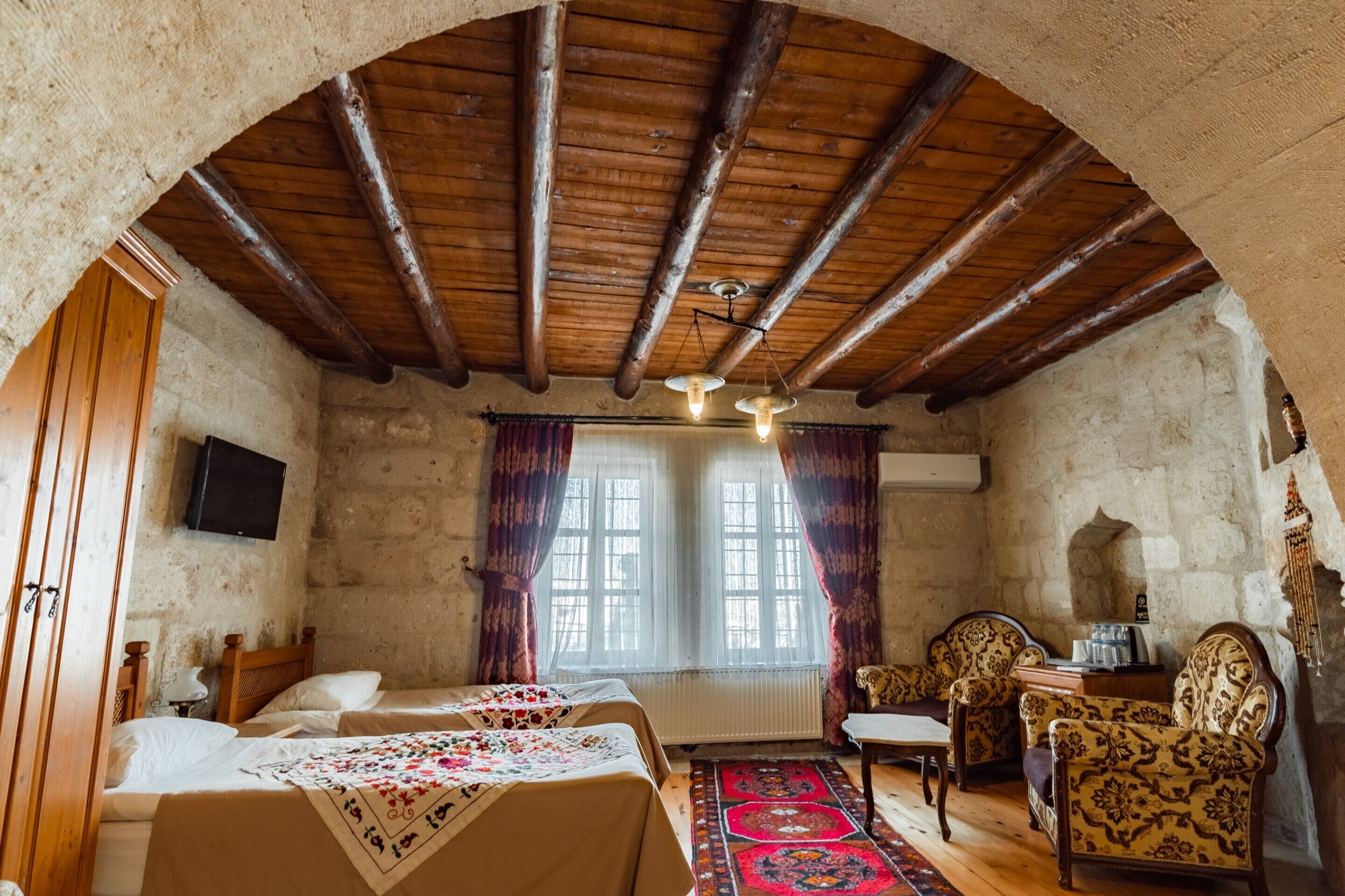 A rustic room with wooden beams, a bed with a floral bedspread, a chair, and a table.