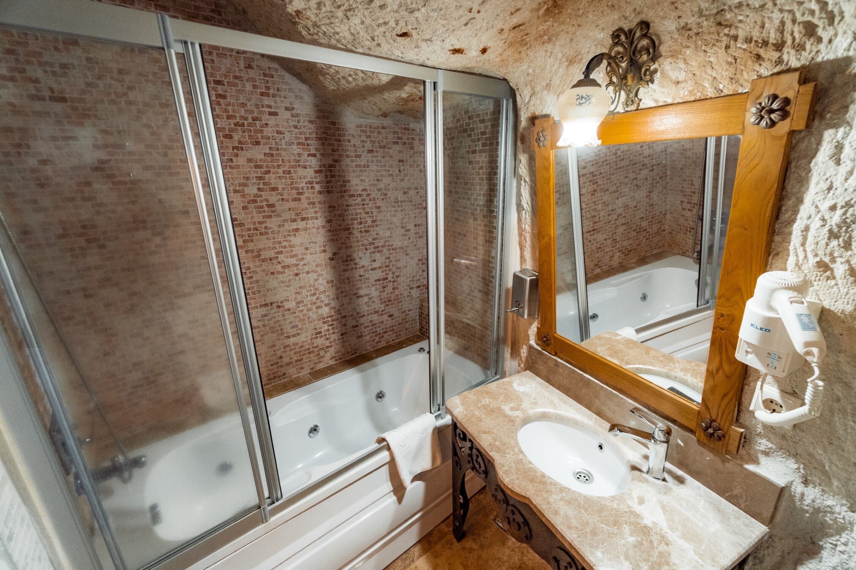 A bathroom with a glass-enclosed shower, a wooden-framed mirror, and a sink with a marble countertop.