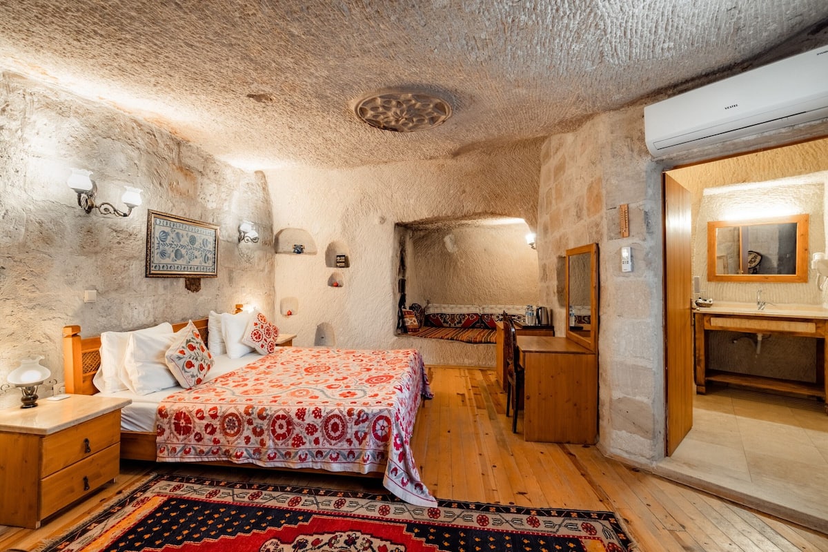 A bedroom with a bed, wooden nightstands, a dresser, a mirror, and a patterned rug.