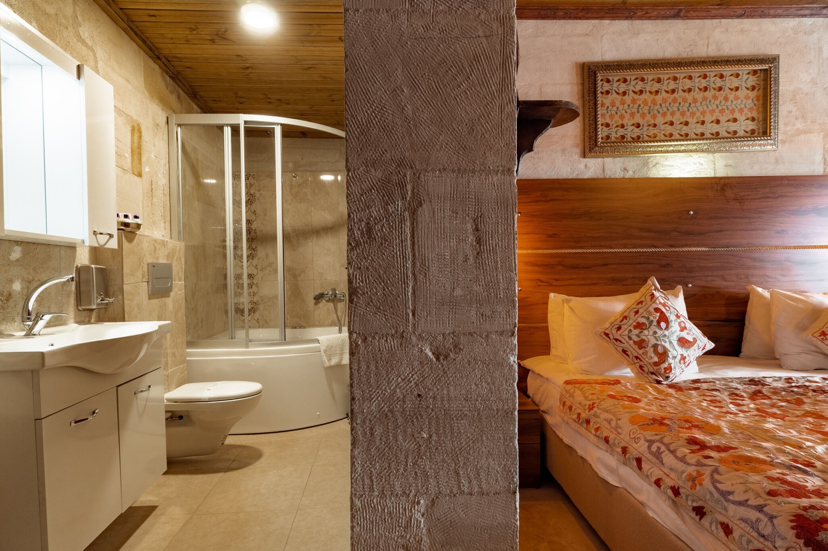 A bathroom with a shower, toilet, sink, and a bed with a patterned bedspread and pillows.
