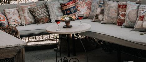 A rooftop seating area with a sofa and table, a potted plant, and a view of a cityscape with unique rock formations.