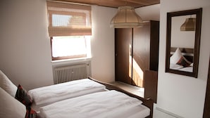 Un dormitorio con dos camas, una ventana con persianas, un radiador, un armario de madera y una lámpara colgante.
