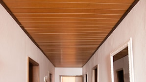 Un pasillo con paneles de techo de madera, suelo alfombrado y puertas que dan a varias habitaciones.