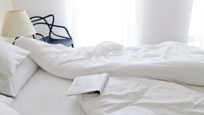 A neatly made bed with white linens, a lamp, and a chair in a bright room with sheer curtains. - Gold Apartments (Wroclaw)