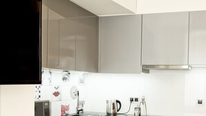A modern kitchen with grey cabinets, a black countertop, and a flat-screen TV mounted above the sink. - Gold Apartments (Wroclaw)