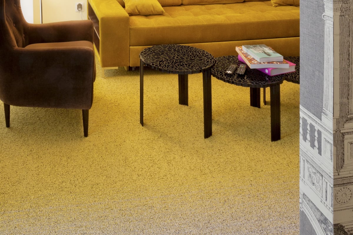 Ein Wohnzimmer mit einem senfgelben Sofa, einem braunen Sessel und einem schwarzen Couchtisch mit Büchern.