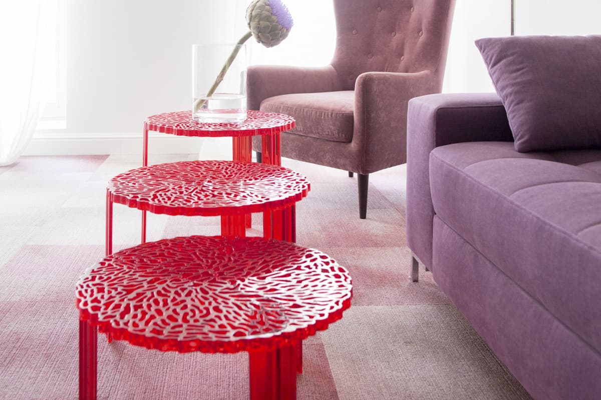 Ein modernes Wohnzimmer mit einem violetten Sofa, einem Tisch mit rotem und weißem Muster und einer roten Lampe.
