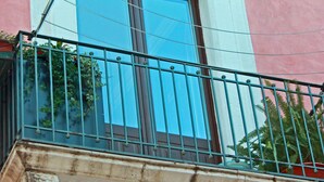 A balcony with a metal railing, a window with a white frame, and a pink wall.