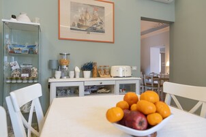 Zona pranzo con tavolo apparecchiato per due, una ciotola di frutta, una vetrina con oggetti decorativi e un quadro appeso al muro.