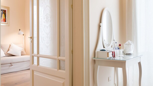 A room with a large mirror, a small table with toiletries, and a white door.