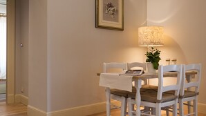A dining area with a table and chairs, a framed picture on the wall, and a lamp.