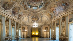 A grand hall with ornate ceiling frescoes, a chandelier, and classical architecture.