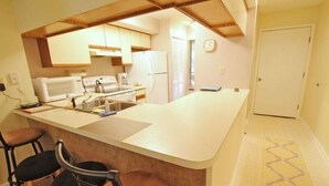 Een compacte keuken met een centraal eiland, barstoelen, een magnetron, fornuis en een koelkast.