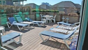 Een houten terras met lounge stoelen en een tafel, omringd door een houten omheining en begroeiing.