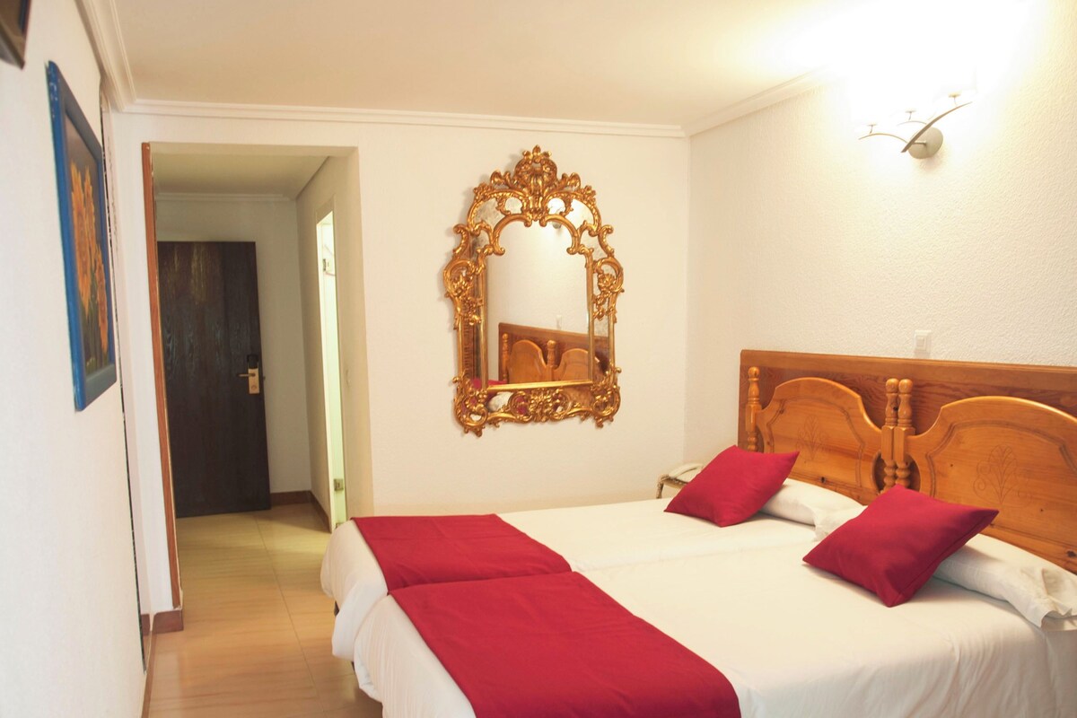 A hotel room with a large bed, a wooden headboard, a mirror, and a red throw blanket.