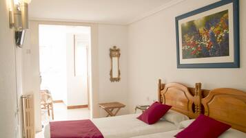 A hotel room with two beds, a wooden headboard, a framed floral painting, and a small table.