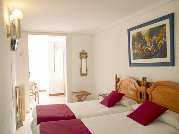 Une chambre d’hôtel avec deux lits, une tête de lit en bois, un tableau floral encadré et une petite table.
