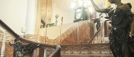 A grand staircase with a statue holding a torch, marble walls, and a chandelier.