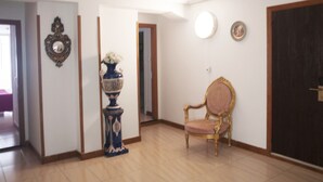 A room with a wooden floor, a decorative blue vase with white flowers, a gold-framed chair, and a door with a dark frame. - Dato 2 (Vitoria-Gasteiz)
