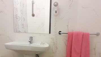 A bathroom with a sink, a bidet, a mirror, a hairdryer, and a basket.